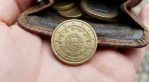 Moneta da 10 centesimi Portogallo 2002 su una mano, con portamonete in pelle e altre monete sullo sfondo