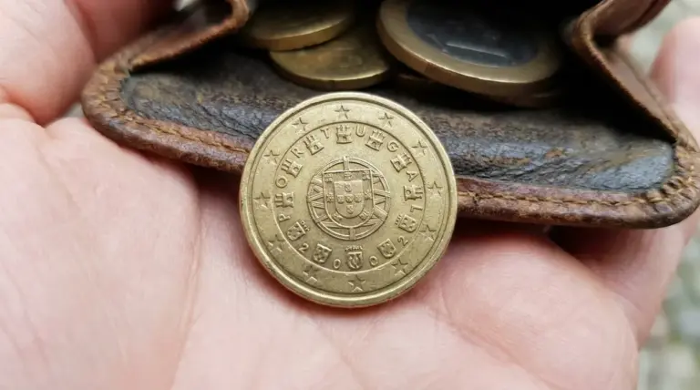 Moneta da 10 centesimi Portogallo 2002 su una mano, con portamonete in pelle e altre monete sullo sfondo