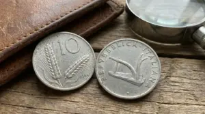 Monete da 10 lire italiane con spiga e aratro su tavolo in legno accanto a portafoglio e lente