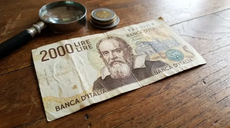 Banconota da 2.000 lire con ritratto di Galileo Galilei su tavolo di legno, con lente d’ingrandimento e monete