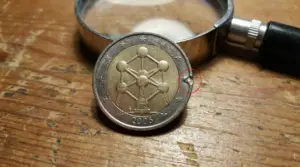 Moneta da 2 euro Belgio 2006 con possibile errore di conio sul bordo, accanto a una lente d’ingrandimento