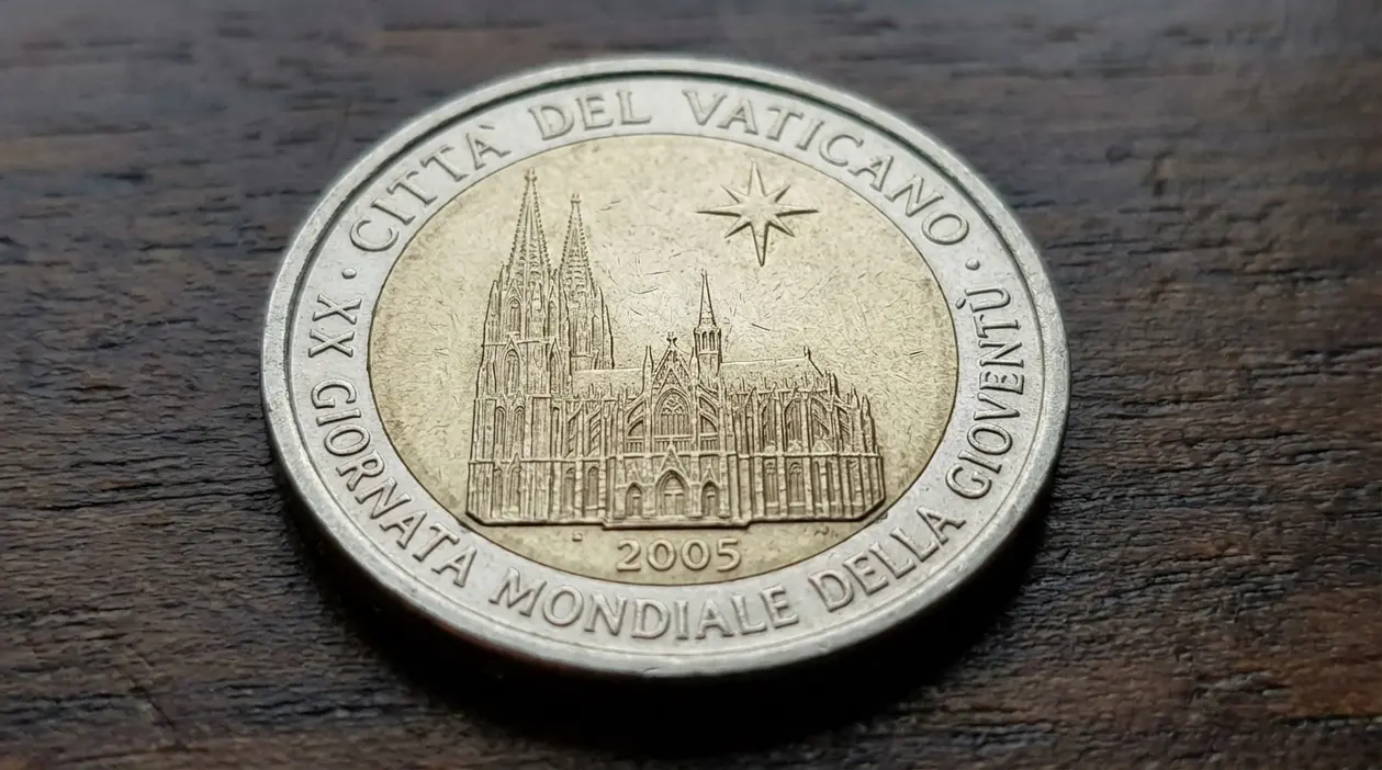 Moneta da 2 euro del Vaticano 2005 con facciata della cattedrale e iscrizione commemorativa, su superficie in legno