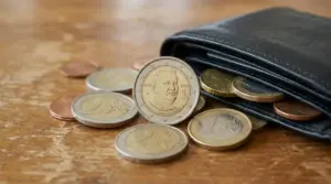 Portafoglio con monete in euro e una moneta da 2 euro dedicata a Giovanni Pascoli in primo piano su un tavolo