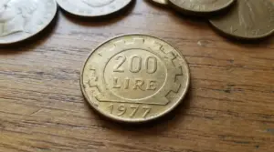 Moneta italiana da 200 lire del 1977 appoggiata su un tavolo di legno, con altre lire sullo sfondo