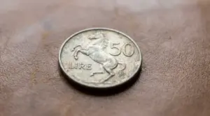 Moneta italiana da 50 lire con cavallino rampante appoggiata su una superficie marrone