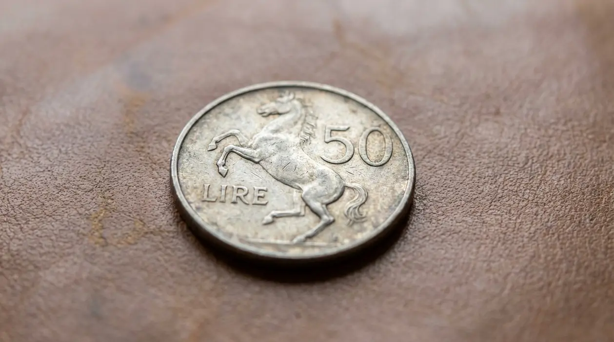 Moneta italiana da 50 lire con cavallino rampante appoggiata su una superficie marrone