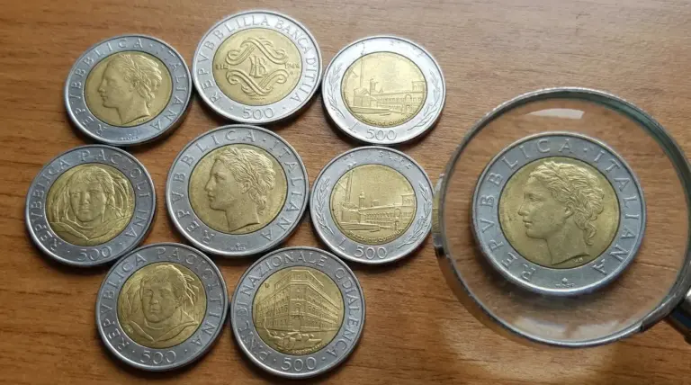 Monete italiane da 500 lire bimetalliche su tavolo in legno, con una osservata attraverso una lente