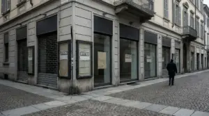 Vetrine di negozio vuoto con cartelli di affitto e vendita in una via cittadina, con una persona che cammina sul marciapiede