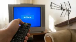Televisore con schermo senza segnale, telecomando in mano e antenna TV sullo sfondo