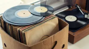 Cassa di cartone piena di dischi in vinile con giradischi sullo sfondo, ideale per valutare una collezione rara