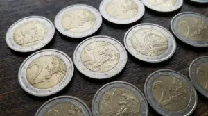 Monete da 2 euro sparse su un tavolo di legno, incluse emissioni commemorative, viste da vicino