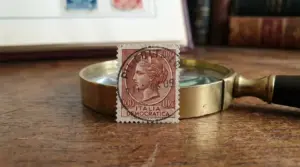 Francobollo Italia “Democratica” da 100 lire su lente d’ingrandimento, appoggiato su un tavolo in legno