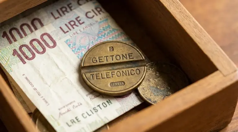 Gettone telefonico d’epoca in un cassetto accanto a una banconota da 1000 lire