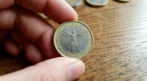 Mano che tiene una moneta da 1 euro rara su un tavolo di legno