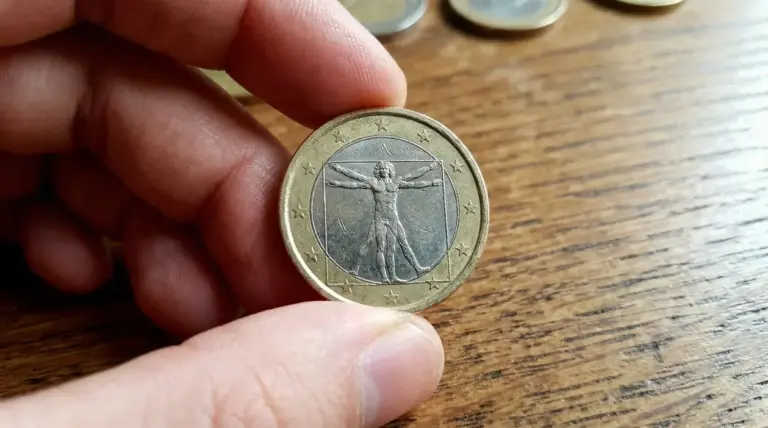 Mano che tiene una moneta da 1 euro rara su un tavolo di legno