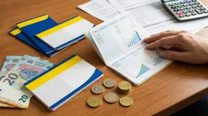 Libretti di risparmio, banconote e monete su un tavolo con una mano che sfoglia un estratto con grafici