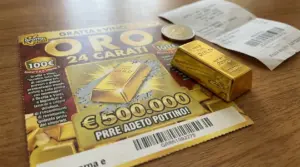 Biglietto Gratta e Vinci Oro 24 Carati con lingotto d’oro, moneta e scontrini su un tavolo