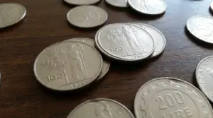 Monete italiane in lire su tavolo di legno, con pezzi da 100 e 200 lire in primo piano