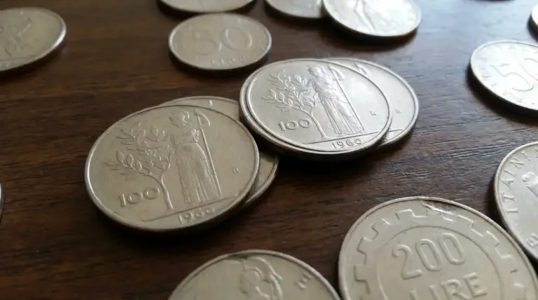 Monete italiane in lire su tavolo di legno, con pezzi da 100 e 200 lire in primo piano