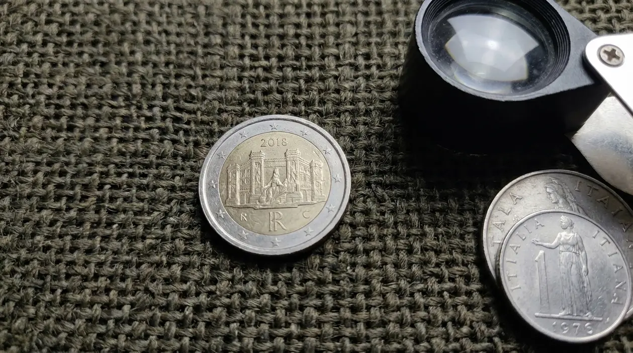 Moneta da 2 euro su tessuto con lente d’ingrandimento e altre monete, tema microerrore e valore di mercato