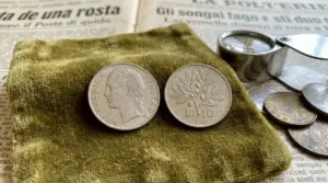 Moneta da 10 lire del 1960 con lente d’ingrandimento e altre monete su panno, per valutazione numismatica