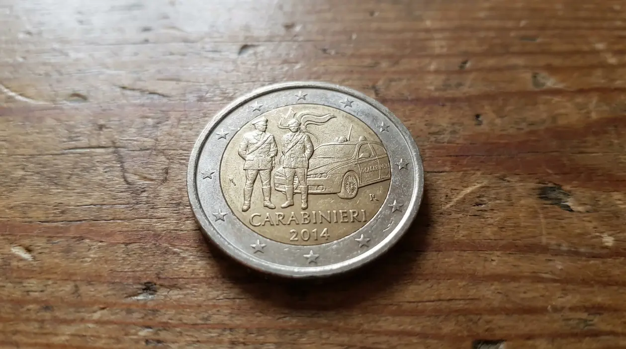 Moneta da 2 euro commemorativa Carabinieri 2014 su superficie di legno, con due figure e auto delle forze dell’ordine