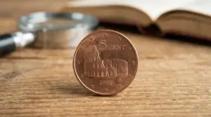 Moneta italiana da 5 centesimi con il Colosseo appoggiata su un tavolo, con lente e libro sullo sfondo