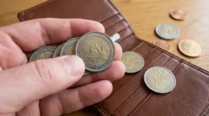 Mano con monete da 2 euro commemorative vicino a un portafoglio aperto su un tavolo