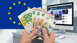 Mani che mostrano banconote in euro davanti alla bandiera UE e a un computer con notizie finanziarie