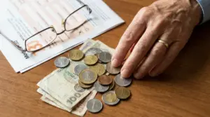 Mano di una persona anziana con occhiali, monete e banconote su documenti, tema pensione e tasse