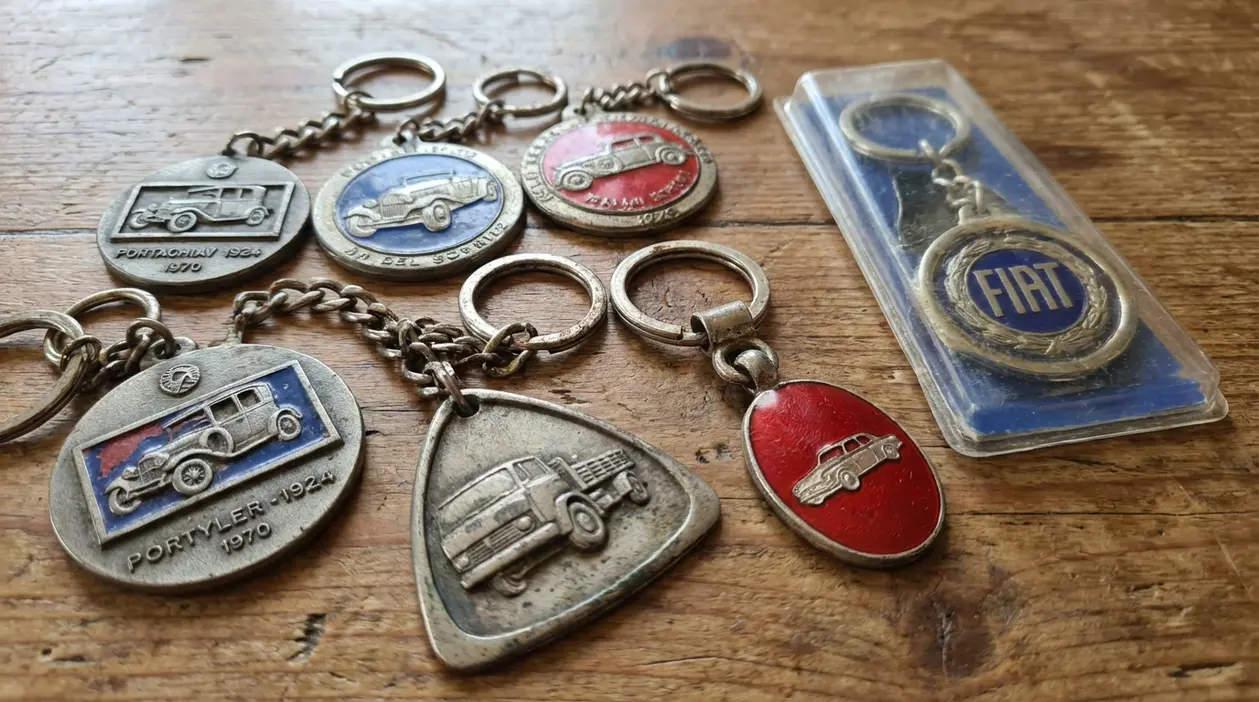 Collezione di portachiavi vintage in metallo con auto d’epoca, appoggiati su un tavolo di legno