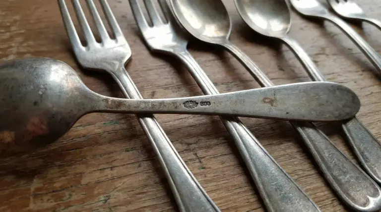 Vecchie posate in alpacca su tavolo di legno con punzone sul manico in primo piano