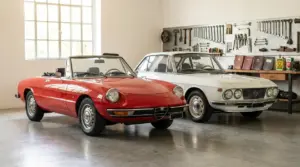 Due auto d’epoca in officina: cabrio rossa e coupé bianca parcheggiate accanto a un banco attrezzi