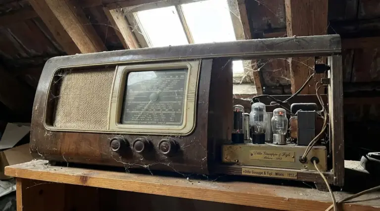 Vecchia radio a valvole anni ’50 impolverata in soffitta, con telaio aperto e componenti interni visibili