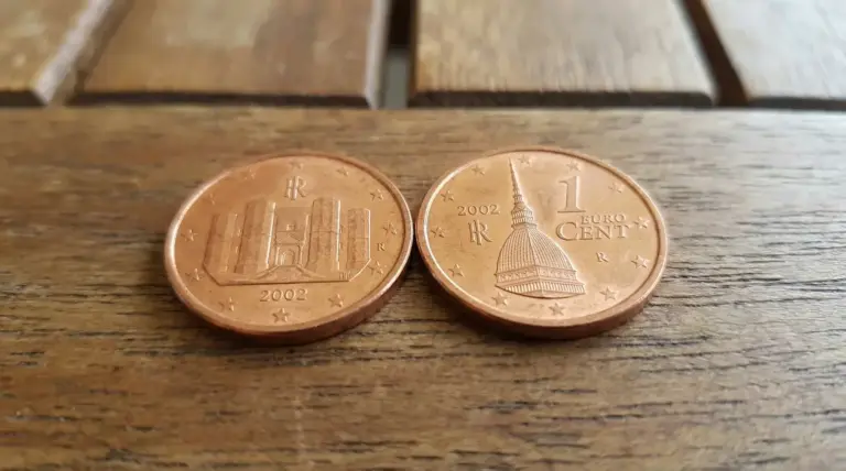 Due monete da 1 centesimo del 2002 appoggiate su un tavolo di legno, fotografate da vicino