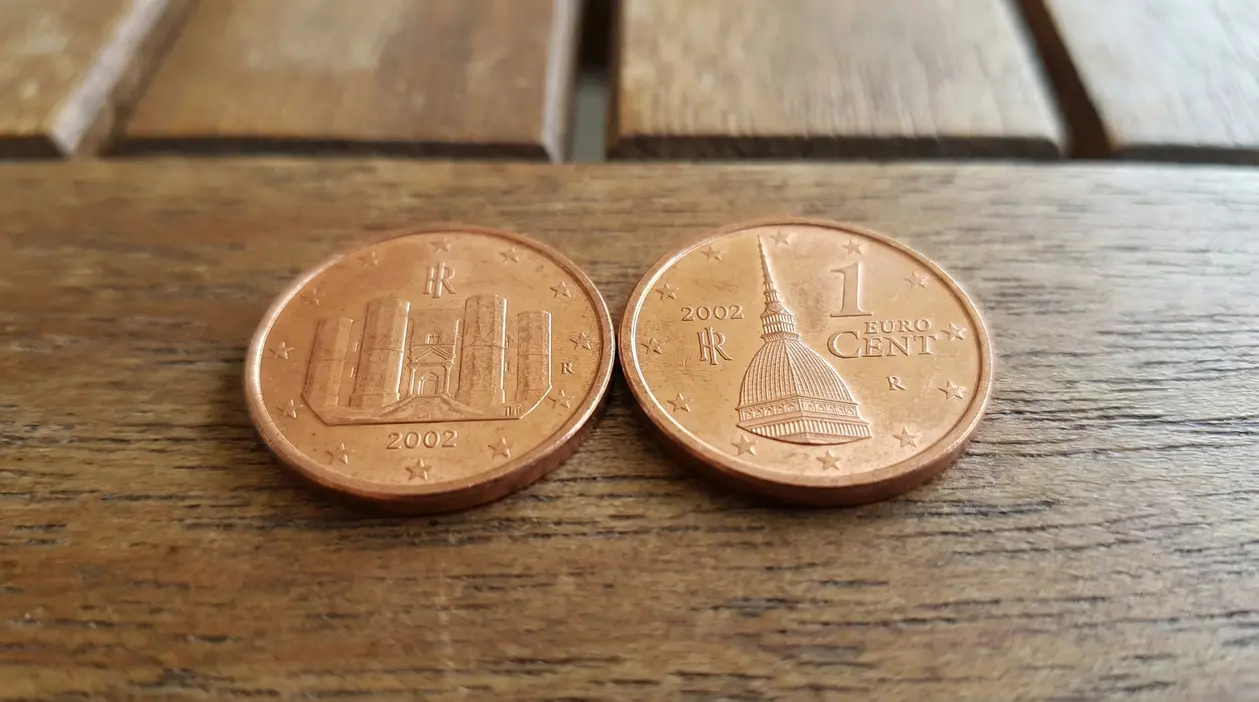 Due monete da 1 centesimo del 2002 appoggiate su un tavolo di legno, fotografate da vicino
