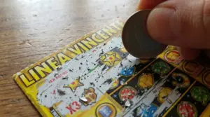 Mano che gratta un gratta e vinci con una moneta, mostrando simboli di gioco su un tavolo di legno