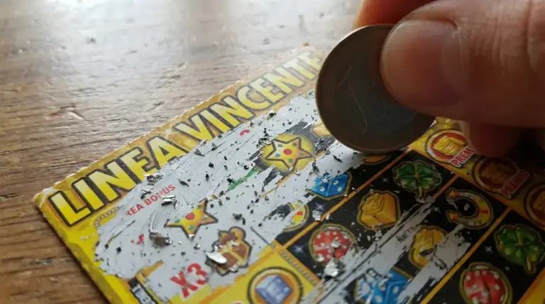 Mano che gratta un gratta e vinci con una moneta, mostrando simboli di gioco su un tavolo di legno