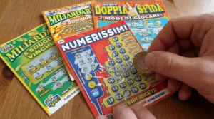 Mano che gratta un biglietto gratta e vinci con una moneta, con altri biglietti sul tavolo
