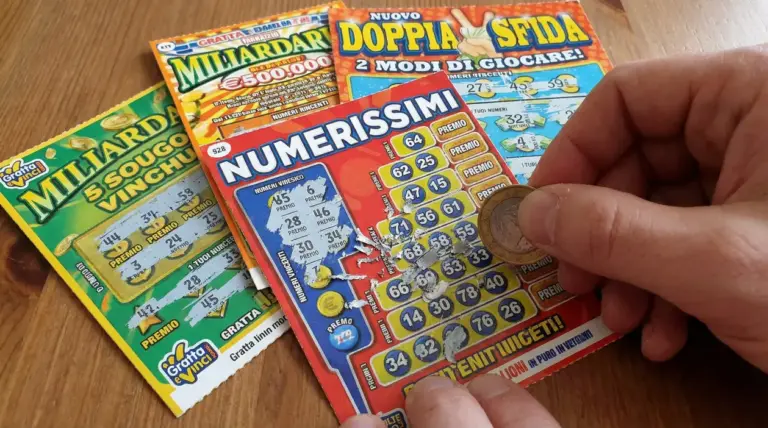 Mano che gratta un biglietto gratta e vinci con una moneta, con altri biglietti sul tavolo