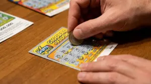 Persona che gratta un biglietto Gratta e Vinci con una moneta su un tavolo di legno