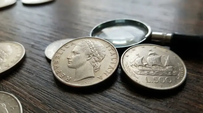 Vecchie monete italiane da 500 lire in argento su un tavolo con lente di ingrandimento