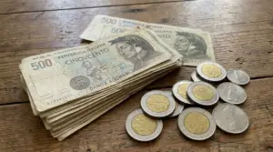 Mazzetta di banconote italiane da 500 lire con alcune monete appoggiate su un tavolo di legno