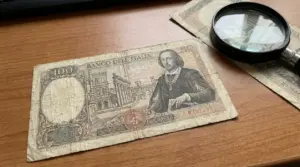 Vecchia banconota italiana da 100 lire su un tavolo, con lente d’ingrandimento per valutarne dettagli e rarità
