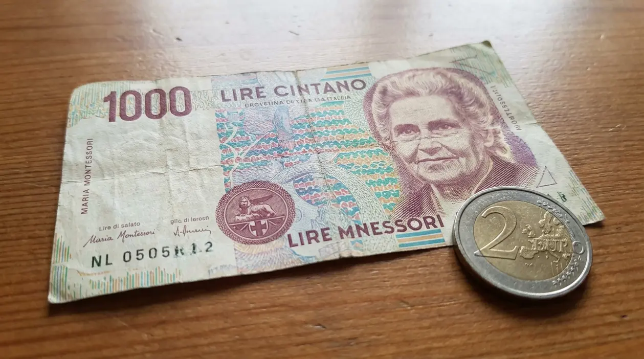 Banconota da 1000 lire Montessori su tavolo in legno, accanto a una moneta da 2 euro