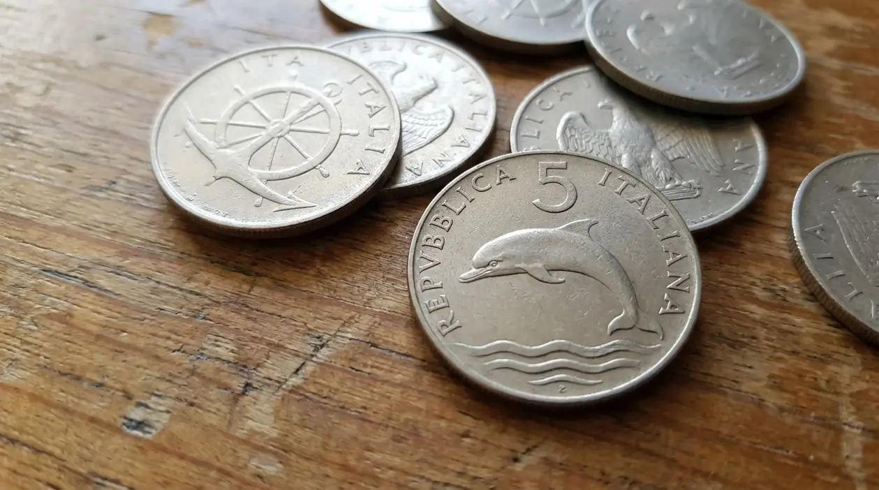 Monete da 5 lire con il delfino della Repubblica Italiana appoggiate su un tavolo di legno