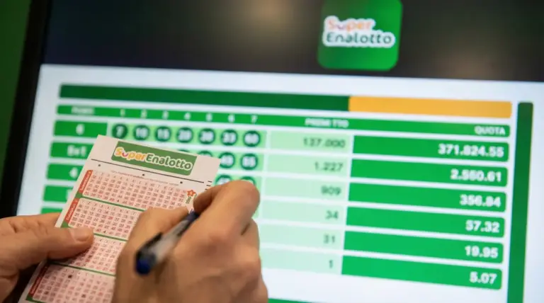 Mano che compila una schedina del SuperEnalotto davanti a uno schermo con risultati e quote di vincita