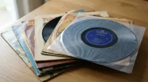 Pila di dischi in vinile con copertine vintage su un tavolo di legno, uno parzialmente estratto dalla busta protettiva