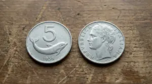 Due monete italiane da 5 lire con delfino (1956) su un tavolo di legno, viste fronte e retro