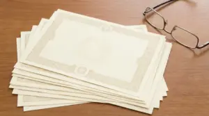 Certificati cartacei impilati su un tavolo di legno con un paio di occhiali, simbolo di investimento sicuro ad alto rendimento